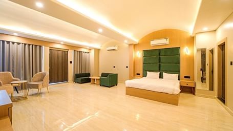 Spacious bedroom at Grassfield Riveria Resort, Jaipur, featuring a large bed, seating area, modern lighting, and floor-to-ceiling curtains.