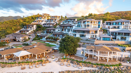 Aerial view of a luxurious hillside beach resort featuring multiple modern villas with balconies