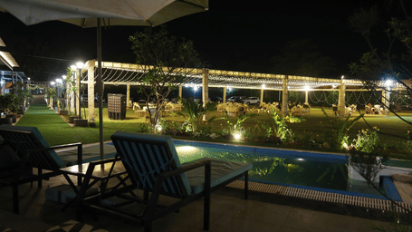 Outdoor seating area at Tisya Farms, Gurgaon with chairs and a poolside view illuminated at night.