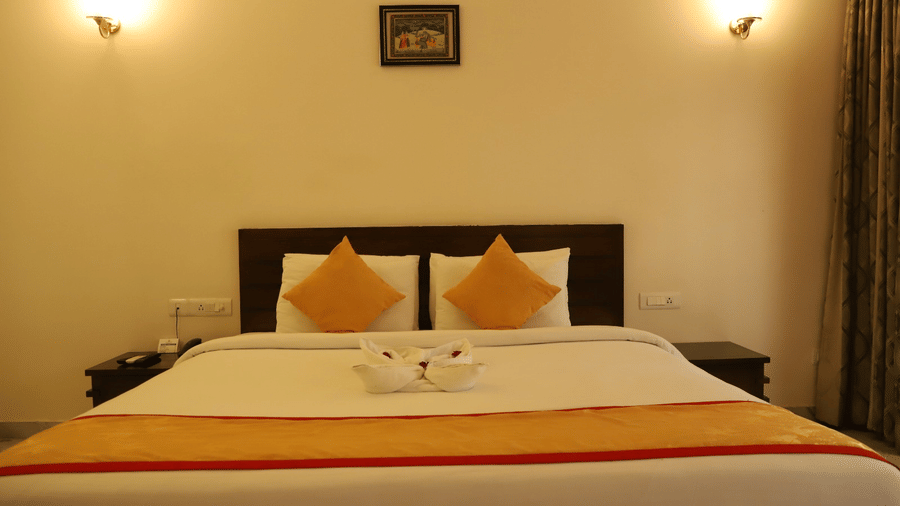 A neatly arranged double bedroom with fresh linens and soft lighting at AS Hotels, Khajuraho.