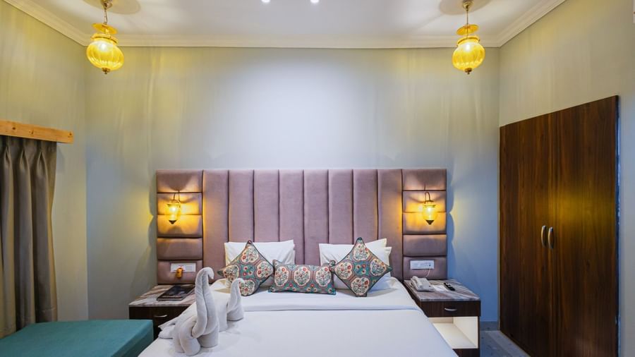 Double bed at Bamboo Saa Resort & Spa, Udaipur with upholstered headboard and towel figurines.
