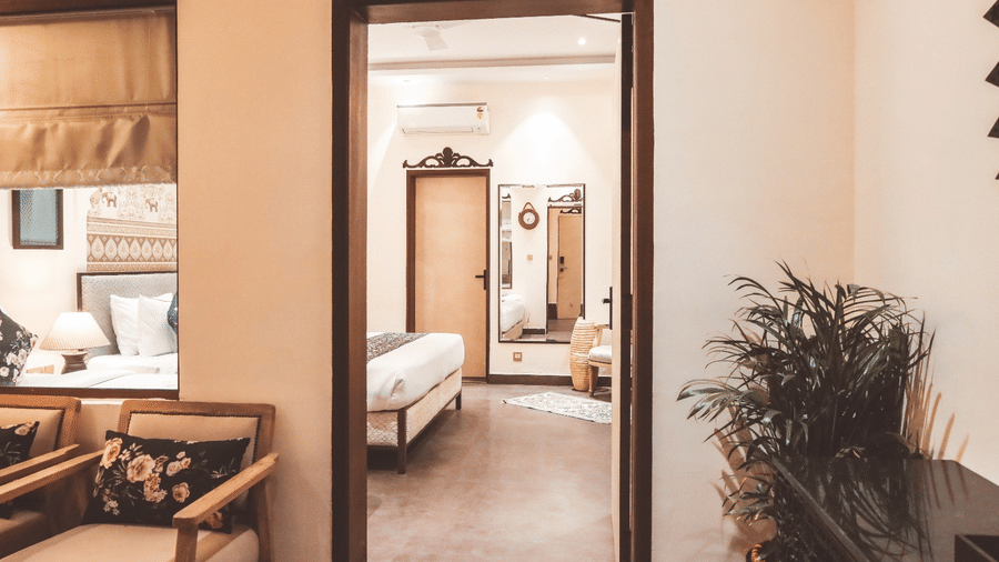 Corridor view leading to bedroom with plants and wooden furniture at Beelwa Palace, Jaipur
