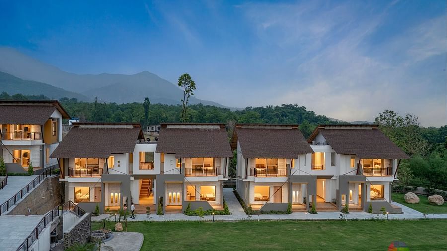 A row of luxurious villas with lit windows, surrounded by lush greenery and mountains in the distance.