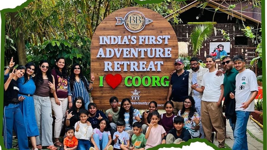 A group of people happily posing in front of a huge wooden board reading Indias First Adventure Retreat and I Love Coorg