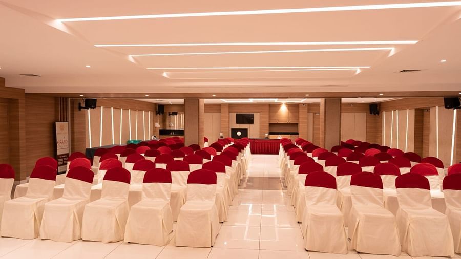 An event hall with white chairs facing the stage at Grand Ashok, Thanjavur.