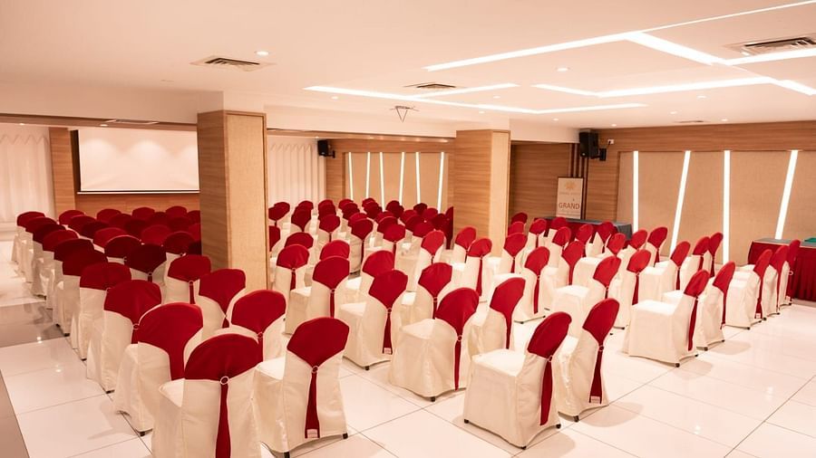 An event hall with white chairs facing the stage at Grand Ashok, Thanjavur.