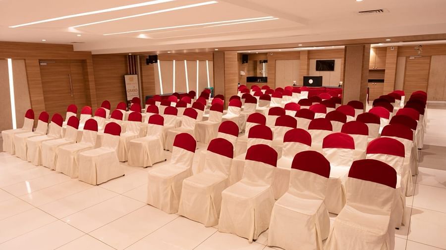 An event hall with white chairs facing the stage at Grand Ashok, Thanjavur.