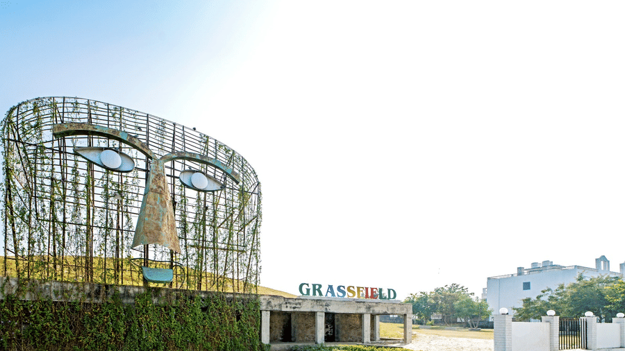 Greenery-covered mask sculpture and signage at the entrance of Grassfield Riviera Resort near Jaipur.
