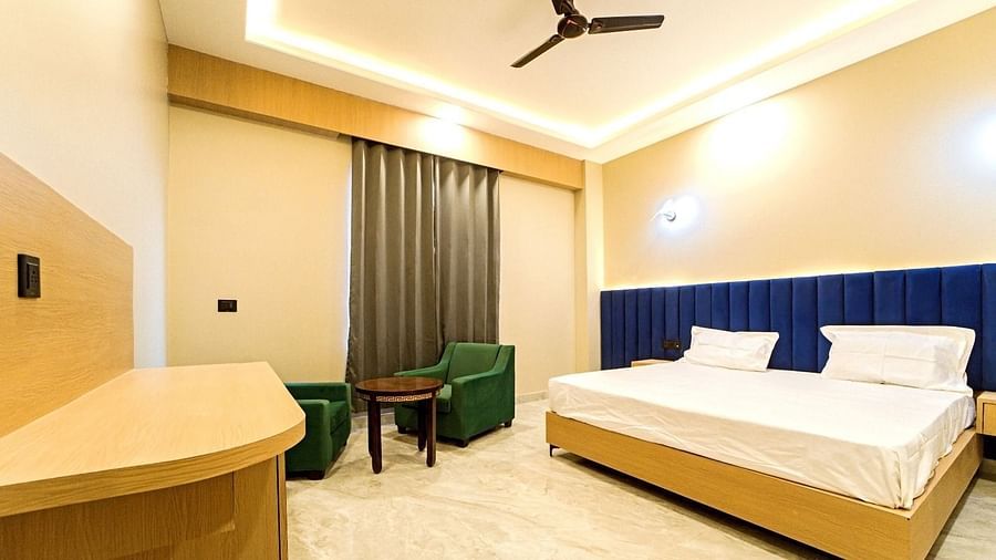 Modern guest room at Grassfield Riveria Resort, Jaipur, featuring a large bed, seating area, ceiling fan, and warm lighting.