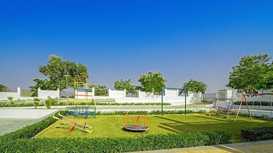 Children’s playground at Grassfield Riveria Resort, Jaipur, featuring swings, a roundabout, and lush greenery under a clear blue sky.