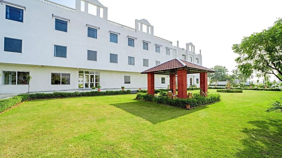 A lawn with a small red gazebo in front of a modern white building at Grassfield Riveria Resort, Jaipur.