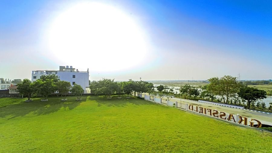 Expansive lawn and buildings at Grassfield Riveria Resort, Jaipur, under a bright sky with distant landscape views.