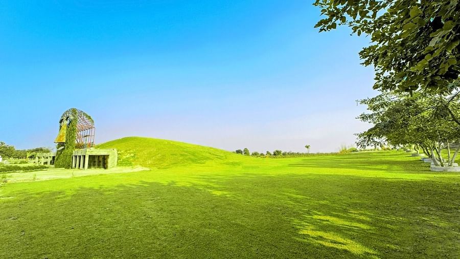 Vast lawn with the artistic mask sculpture of Grassfield Riveria Resort, Jaipur, set against a clear sky.