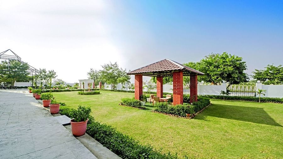 Tranquil garden area at Grassfield Riveria Resort, Jaipur, featuring a small gazebo, manicured lawns, and potted plants along the pathway.
