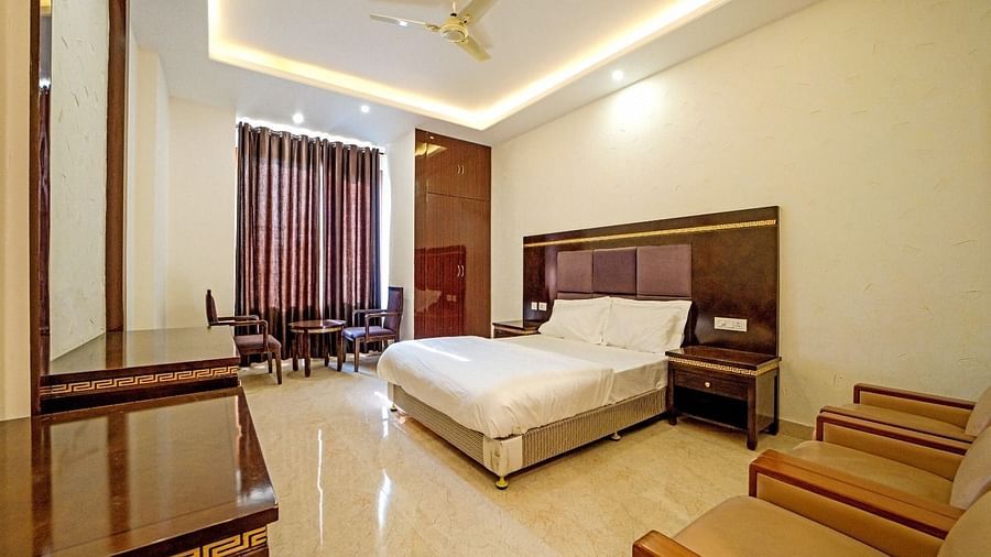 Elegant bedroom at Grassfield Riveria Resort, Jaipur, featuring a large bed, wooden furniture, and warm ambient lighting.