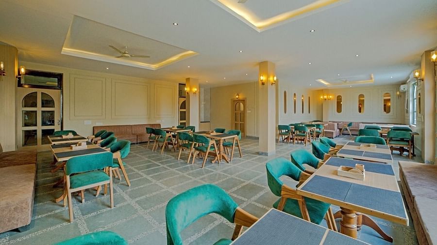 Elegant dining area at Grassfield Riveria Resort, Jaipur, with teal upholstered chairs, wooden tables, and warm lighting.