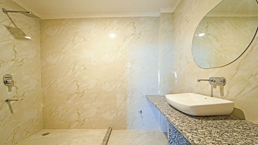 Contemporary bathroom at Grassfield Riveria Resort, Jaipur, with a walk-in shower, round mirror, and sleek countertop basin.