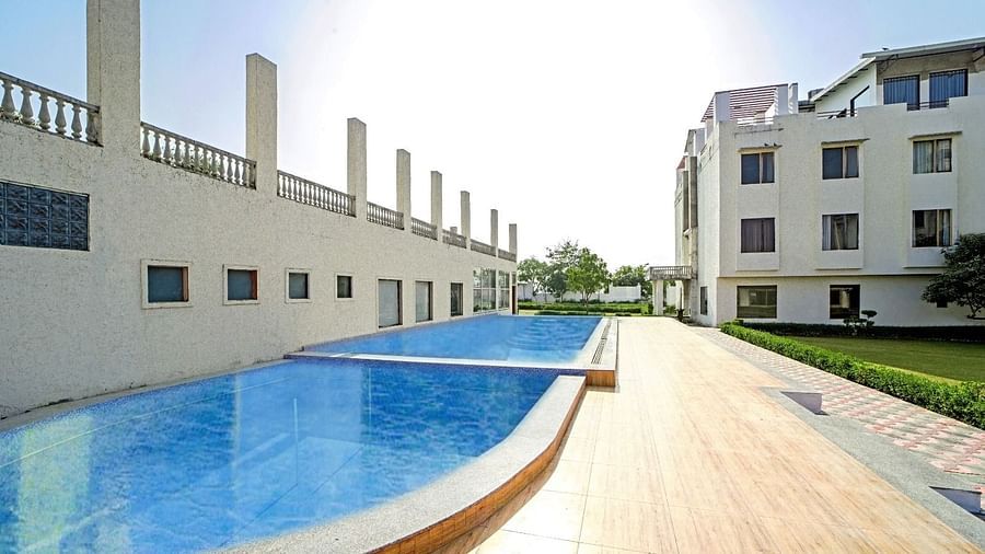 Outdoor swimming pool at Grassfield Riveria Resort, Jaipur, featuring clear water and a wooden deck under bright sunlight.