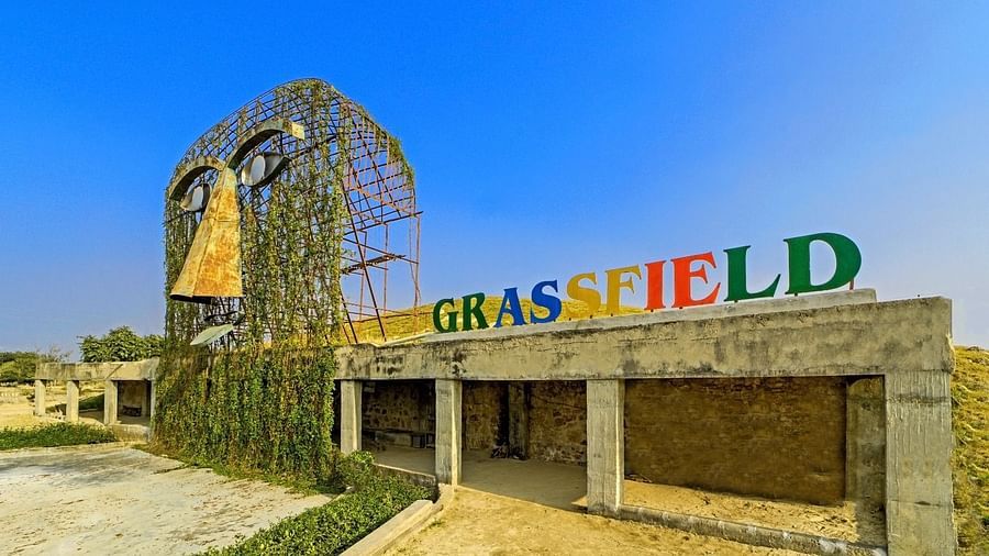 Entrance of Grassfield Riveria Resort, Jaipur, featuring a large artistic mask sculpture covered with greenery and colourful signage.