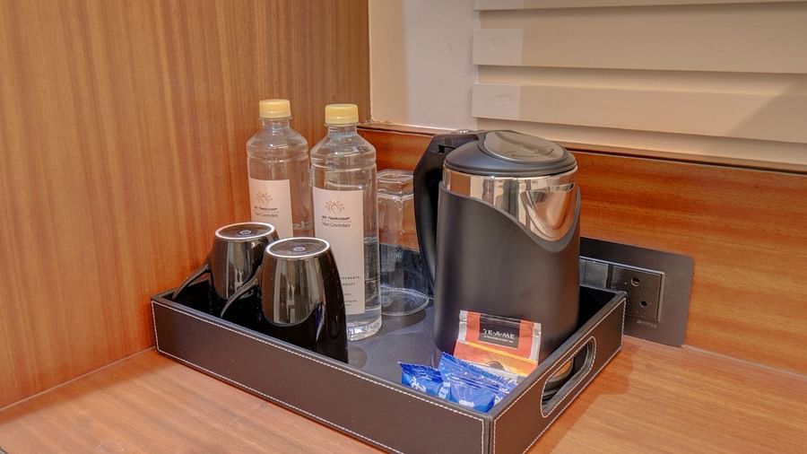 An image of a flat surface with a tray containing two water bottles, a kettle, two cups, and packets of milk and tea at Hari Govindas, Siddappa Square.