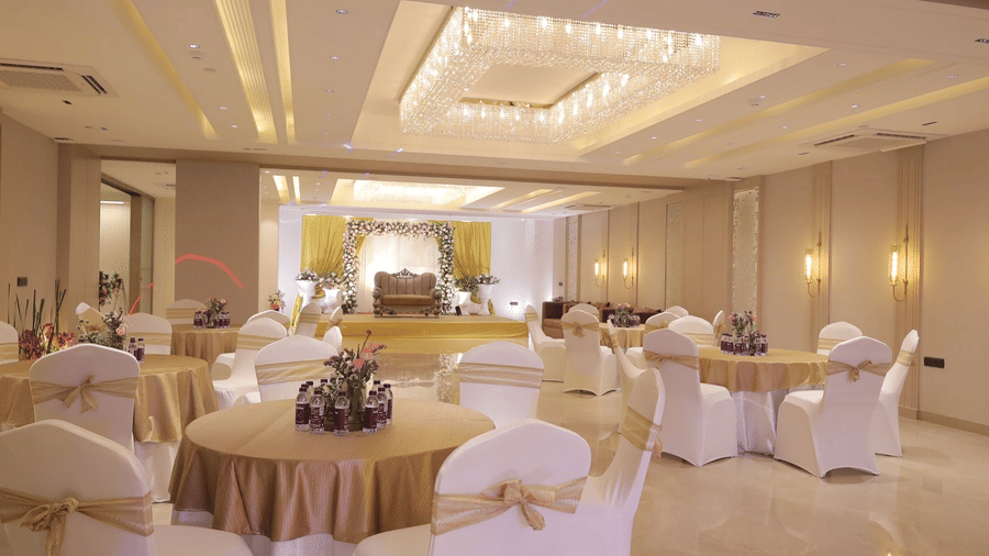 The brightly lit interiors of the Crystal Hall at Hotel 91 Privé, Gurugram, featuring a beautiful false ceiling along with tables and chairs arranged in round table configuration.