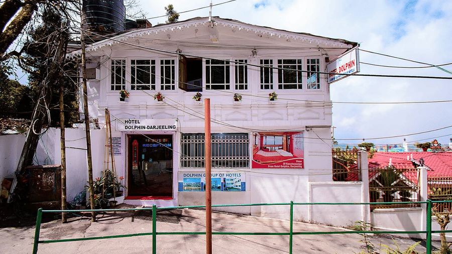A 2-storey white guesthouse with a green railing and a light blue sky in the background at Hotel Dolphin Darjeeling.