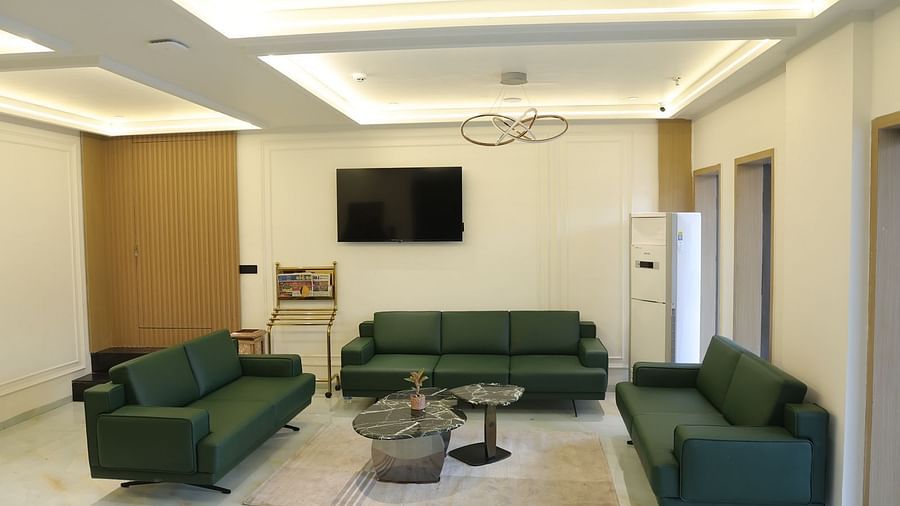 An elegant hotel lobby at Lords Eco inn Jamnagar Maheshwari Nagar with green sofas a coffee table and a large television.