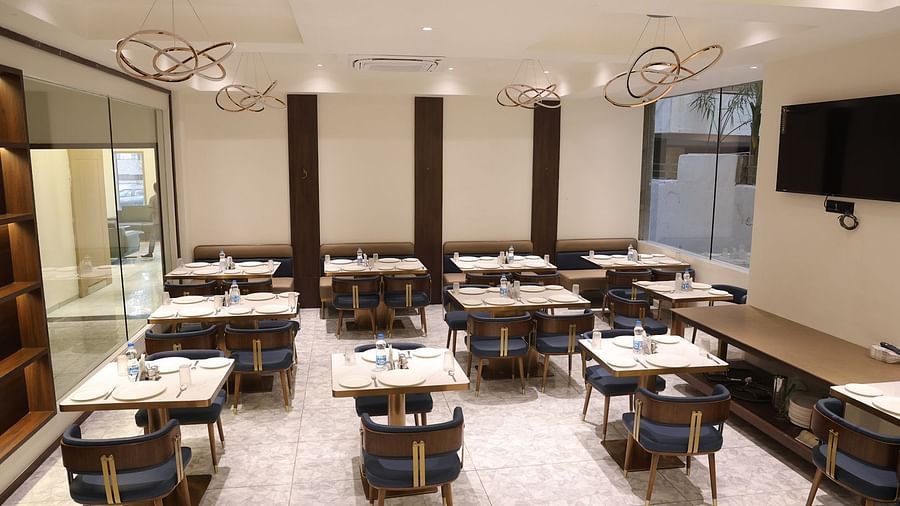 A brightly lit dining area at Lords Eco inn Jamnagar Maheshwari Nagar with multiple tables chairs and stylish lighting.