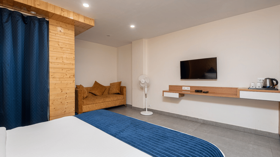 Minimalist bedroom with double bed, blue curtains, wall-mounted TV, and minimalist design at MV Acosta, Mussoorie.