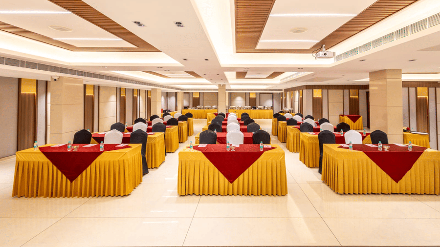 Corporate meeting setup at S Convention Centre of S Hotels, Chennai featuring rows of tables with brightly-coloured linens, oriented towards the front for a presentation or seminar.