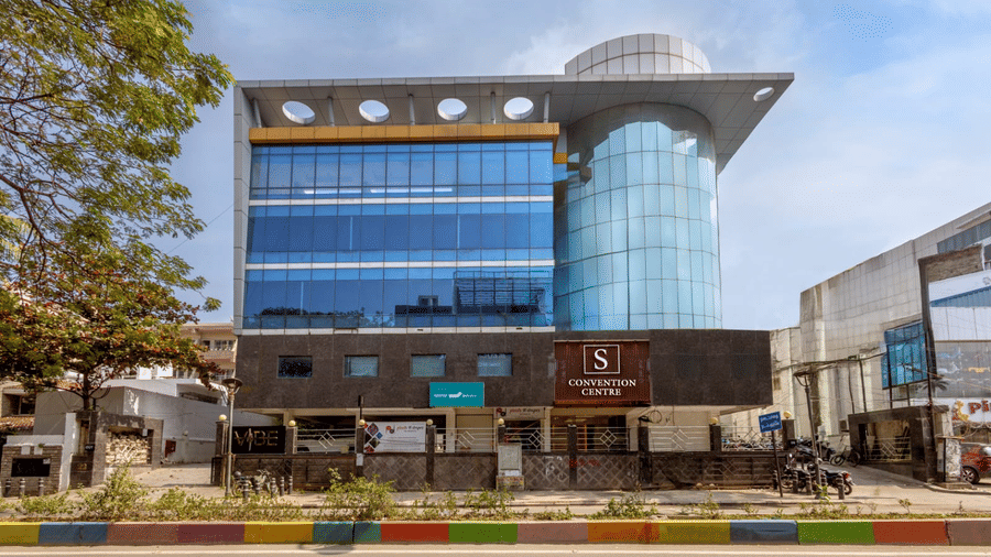 The modern glass exterior of the S Convention Centre of S Hotels, Chennai, showcasing its multi-story architecture and prominent signage.