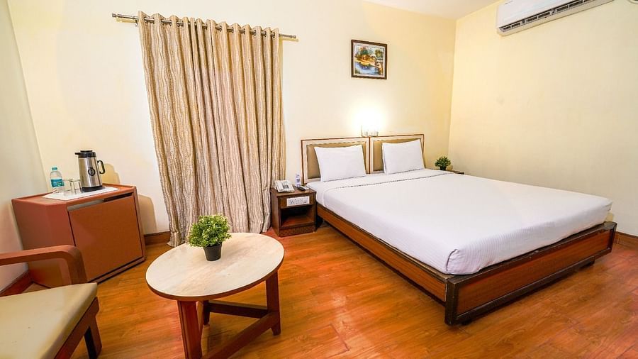 Bright hotel room with a double bed, wooden flooring, and a seating area by the window in Hyderabad near Ramoji Film City.