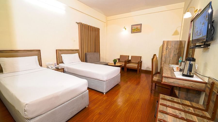 Well-lit hotel room with two single beds, wooden flooring, a spacious seating area, and a flat-screen TV in Hyderabad near Ramoji Film City.