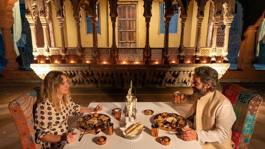 A man and woman in a dining area with an assortment of food placed on the table at Aerial view of a swimming pool with lounge chairs on the side at Surpura Bagh.