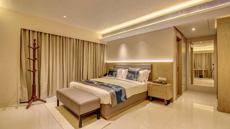 City View Suite at The SSK Solitaire Hotel and Banquets, Mumbai Naka featuring a bed, a wooden stand with branches acting as hangers, bedside table on either side of the bed, and a sneak peak of another room.