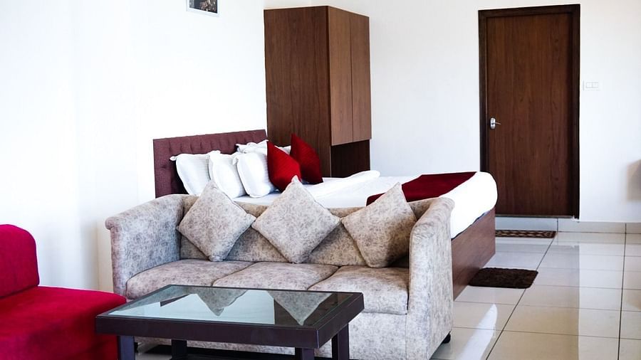 A beige sofa, red armchair, glass coffee table, and a plush bed in the background. | Vistar Resort, Bengaluru