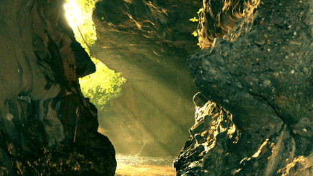 A beam of light shines into a dark cave with rocks.