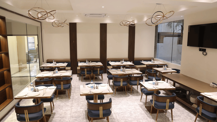 A brightly lit dining area at Blue Coriander at Lords Studio Inn, Jamnagar with multiple tables chairs and stylish lighting.