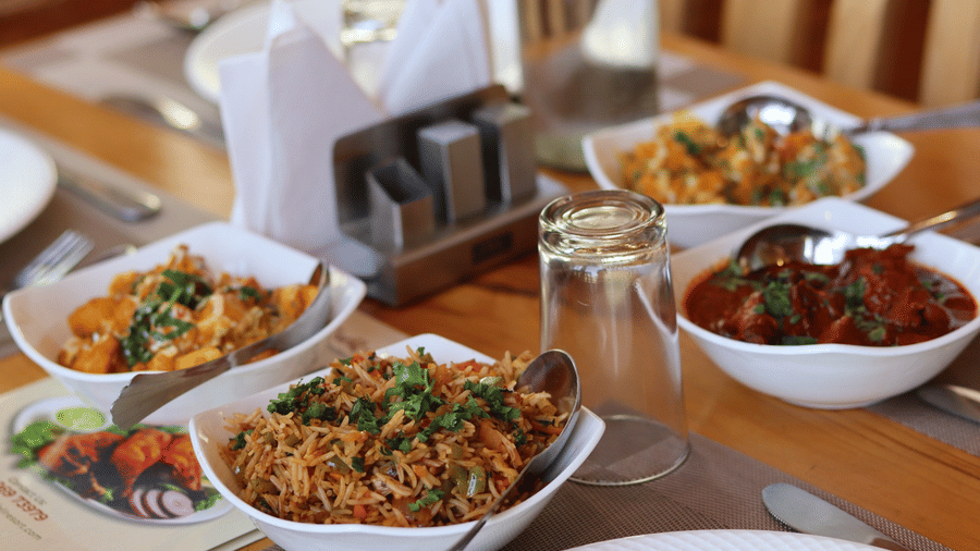 Multiple bowls of food arranged on 1 long dining table with glasses, cutlery and menus at Dawat e Drung by FrozenFall Resort, Drung, Tangmarg.