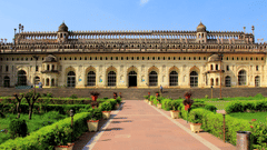 A wide-angle view of a large, beautiful historical palace with a long, stone walkway leading up to it through a green lawn.