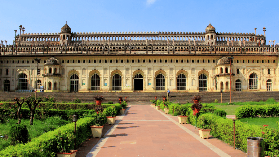 A wide-angle view of a large, beautiful historical palace with a long, stone walkway leading up to it through a green lawn.