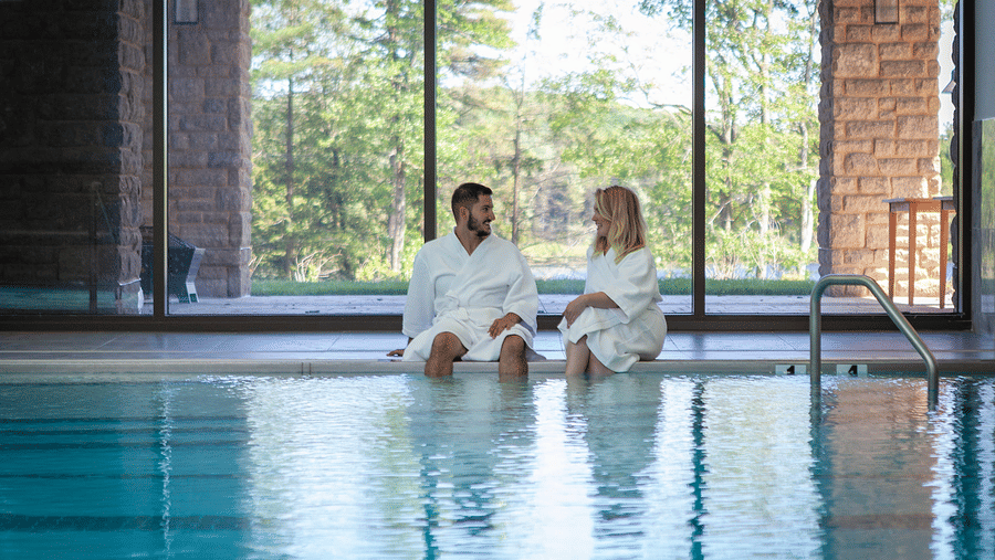 2 individuals in bathrobes interacting with each other at the pool deck with their legs dipped in the water at YO1 Resorts