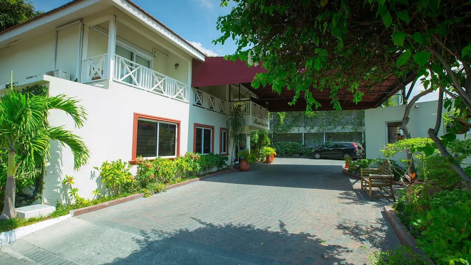 A white house with a roof is seen from a paved driveway leading up to its entrance | Altamont Court, Jamaica