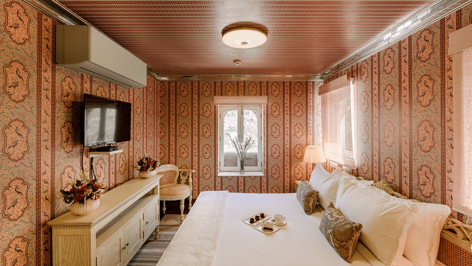 Fancy room at Surya Vilas in Jaipur featuring walls decorated with traditional artwork and a plush bed facing the TV mounted on the wall