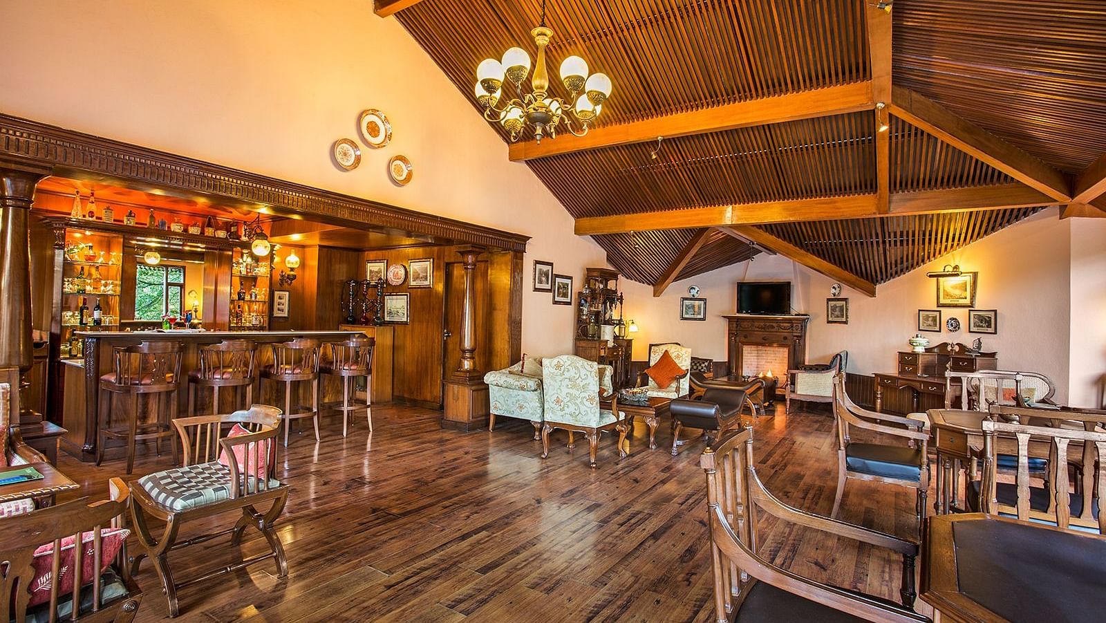 An image of indoor view of the bar at The Naini Retreat, Nainital, with sets of chairs and tables placed around the chandelier on the ceiling.
