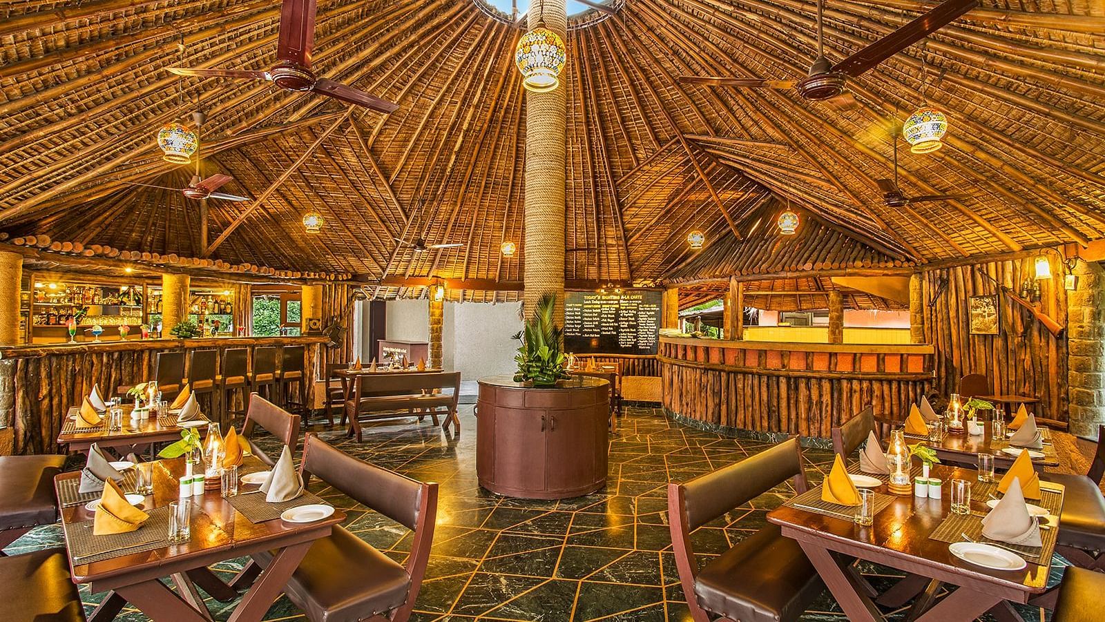 An image of a bar with wooden interiors, wooden chairs and tables, with plants filled at every corner - The Riverview Retreat, Corbett