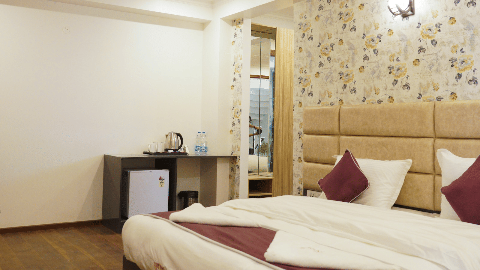 Bedroom of Lime Tree Hotels & Service Apartment Private Limited featuring a padded headboard, a mirrored wardrobe, and maroon bedding.
