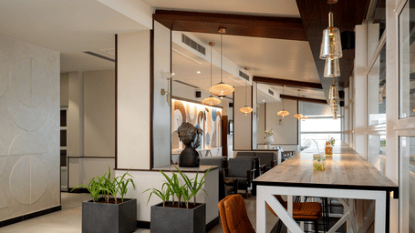 Contemporary dining area with a long wooden table, pendant lights, and potted plants in dark square planters at Hotel Sonar Bangla, Puri.
