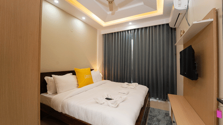 Bedroom of Lime Tree Hotels & Service Apartment Private Limited featuring striped curtains, a wall mounted television, and white bedding.