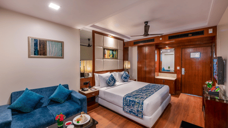 a queen size bed room with ceiling fan, centralised air-conditioning, wall-mounted TV, a seating area for two, and full length mirror at Libra Lords Inn Jaipur 